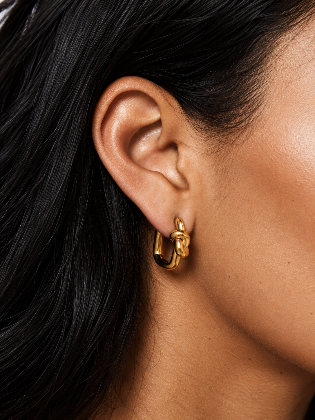 Gold Twine EARRING with a sculpted knot worn in the lobe of a model with sleek dark hair.