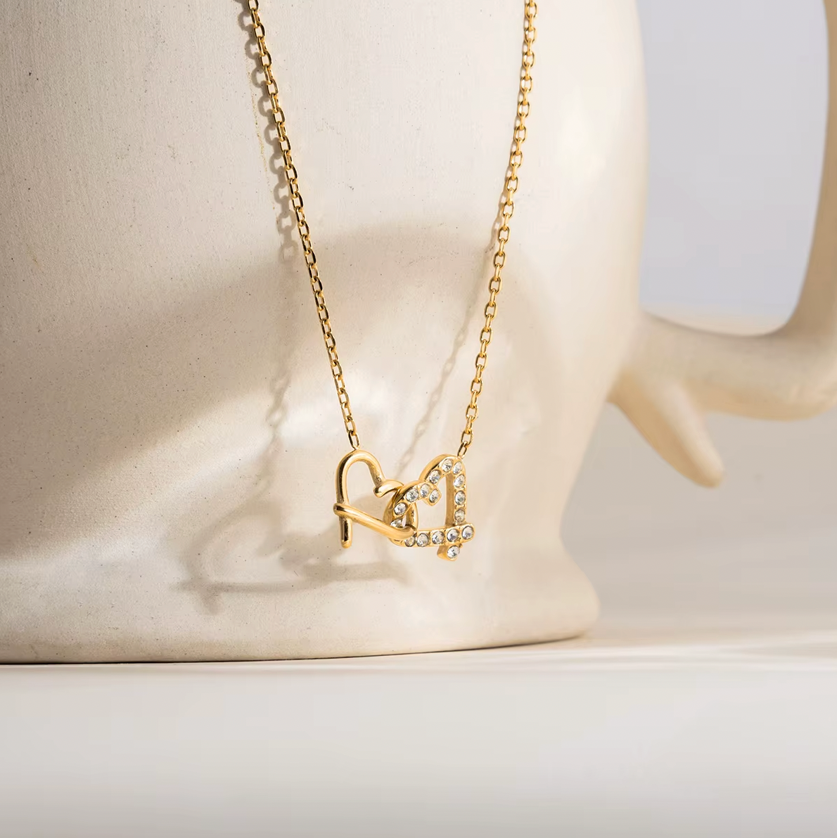 Gold-plated necklace with a delicate chain and interlocking heart-shaped pendant embellished with clear crystals