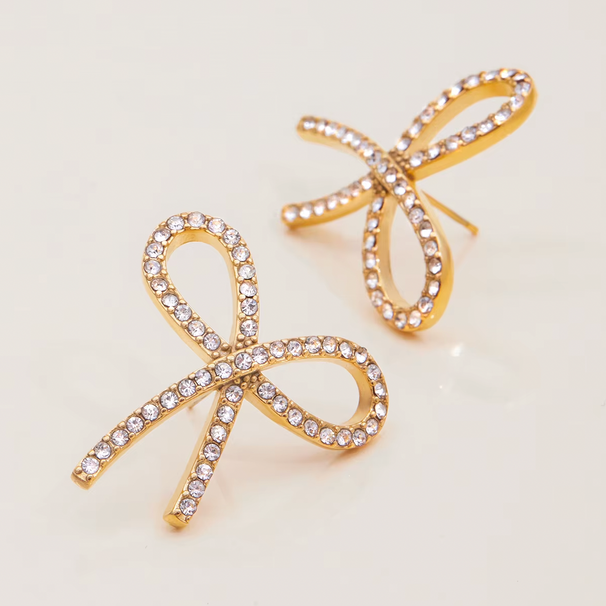Gold-plated bow-shaped stud earrings embellished with clear crystal stones