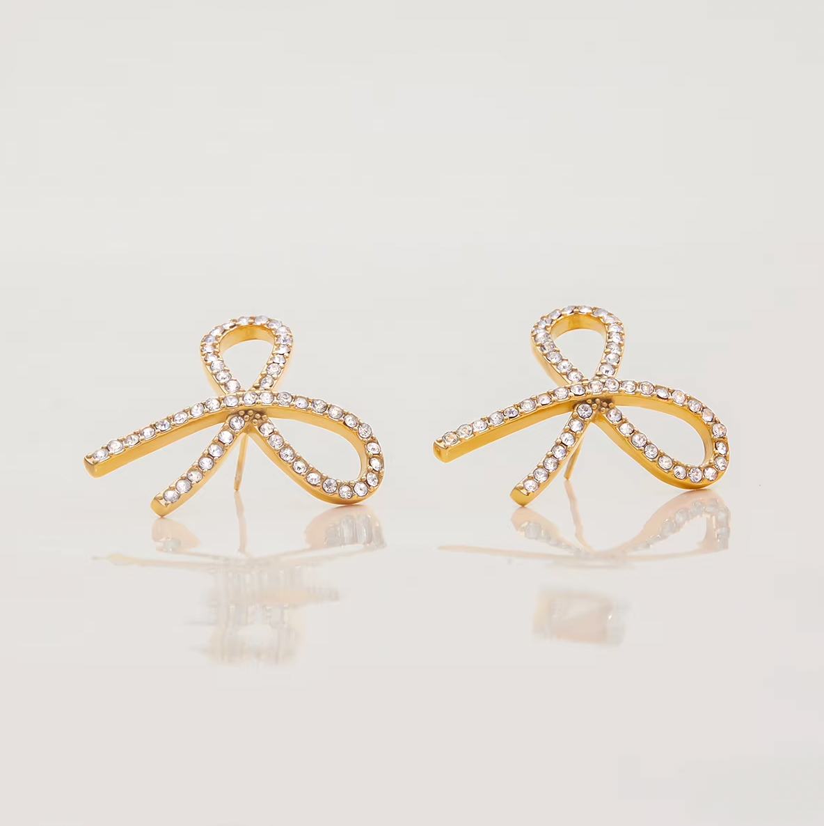 Gold-plated bow-shaped stud earrings embellished with clear crystal stones