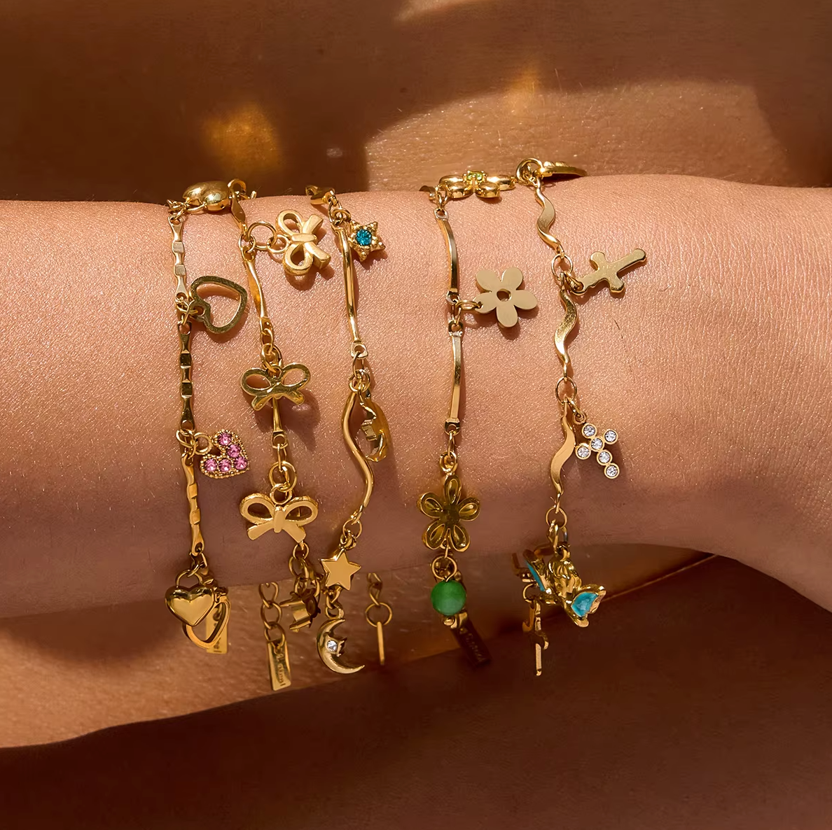 Gold-plated charm bracelet with multiple heart-shaped charms, including open hearts, polished gold hearts, and a pink crystal heart
