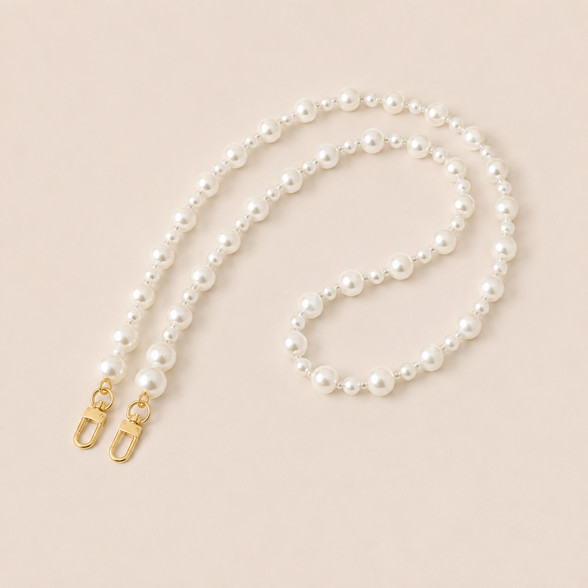 Folie à Trois Adair Pearl long wholesale phone chain in graduated white pearls with gold clasps, coiled on a cream background.