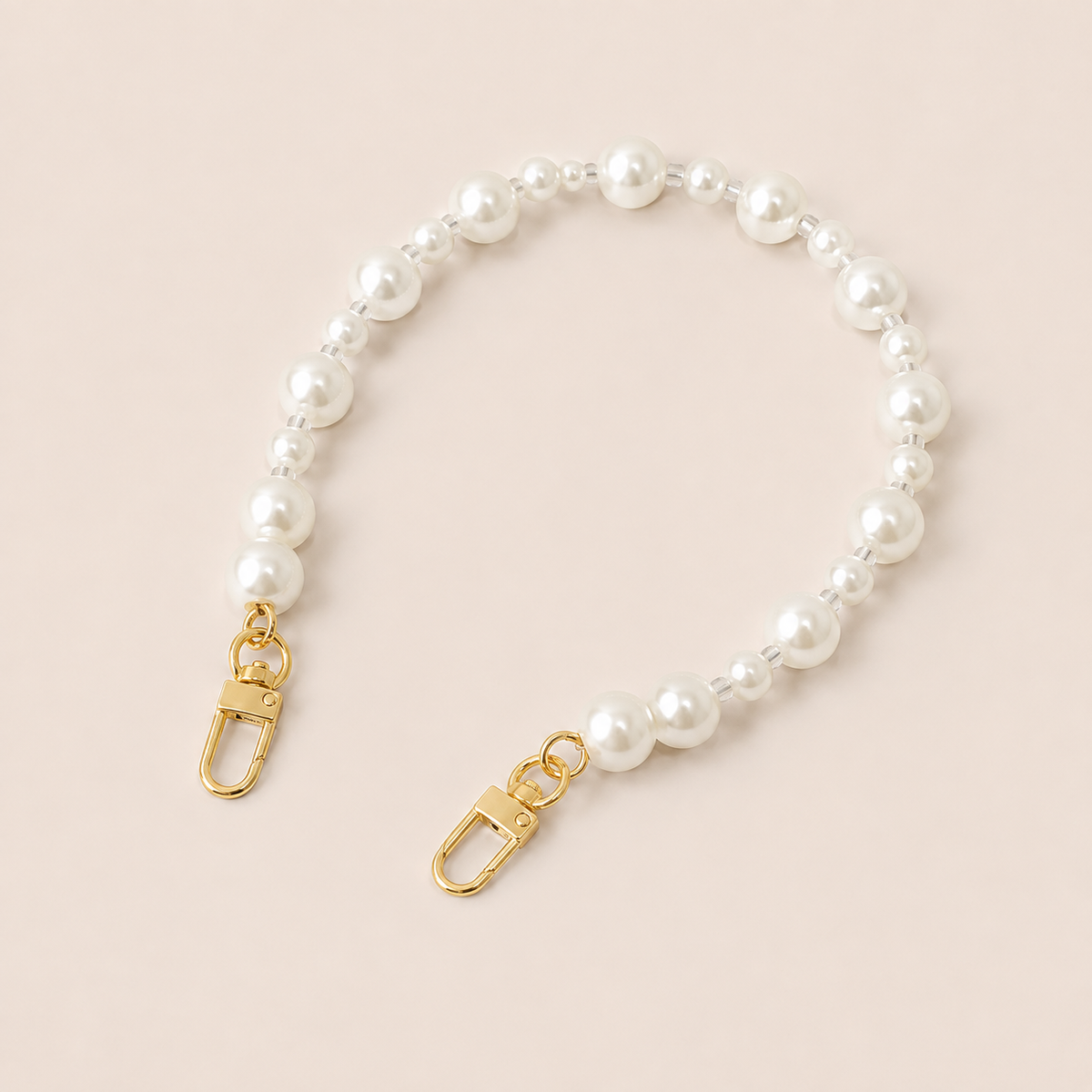 Folie à Trois Adair Pearl short wholesale phone chain in white pearls with clear glass spacers and gold clasps, laid flat on a cream background.