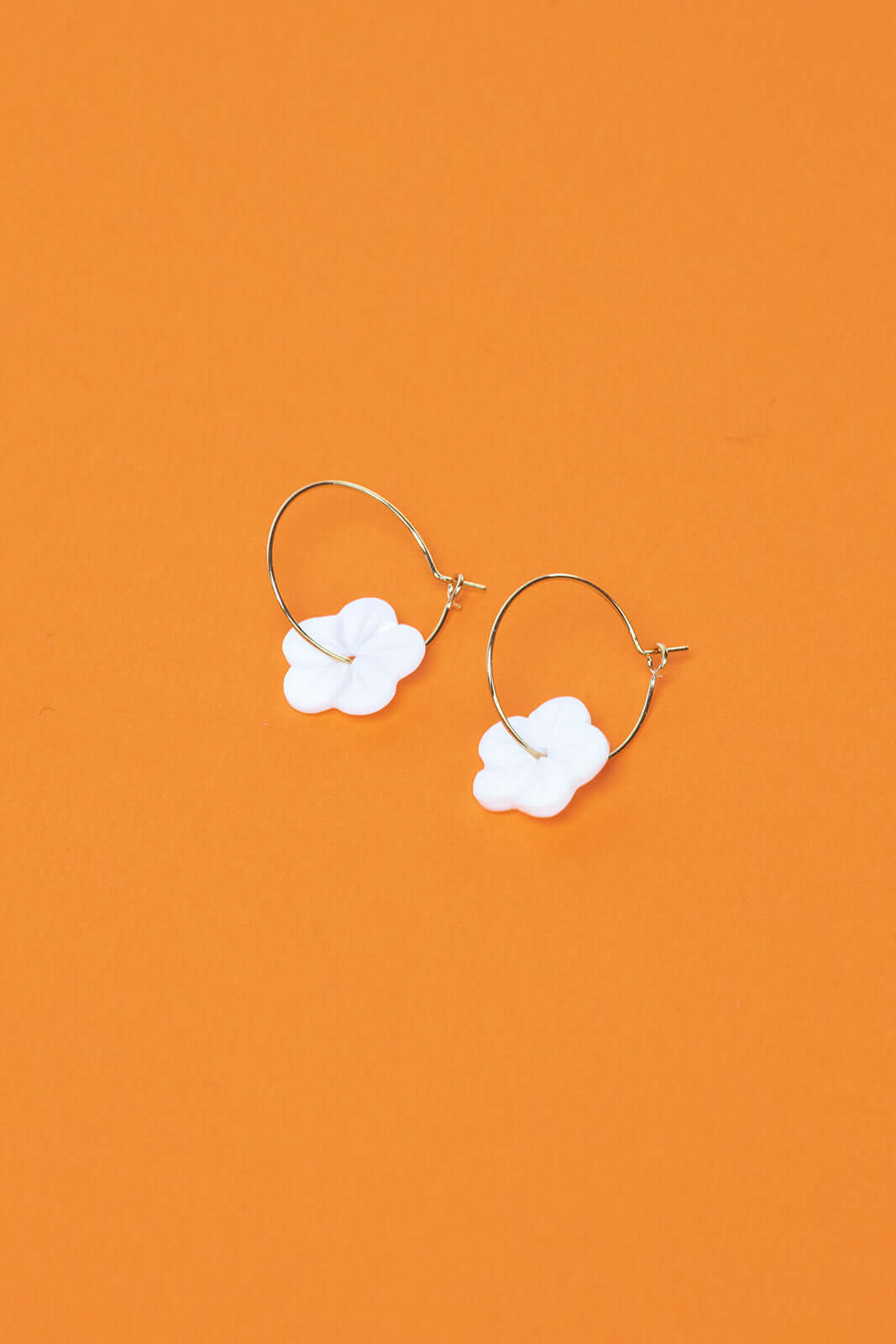 Against a bold orange backdrop, After Glow Earrings show off their white flower bead and slim gold hoop.