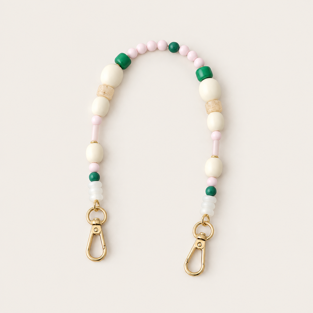 Folie à Trois Alder short wholesale phone chain in cream, pink, green and frosted beads with gold lobster clasps, laid flat on a cream background.