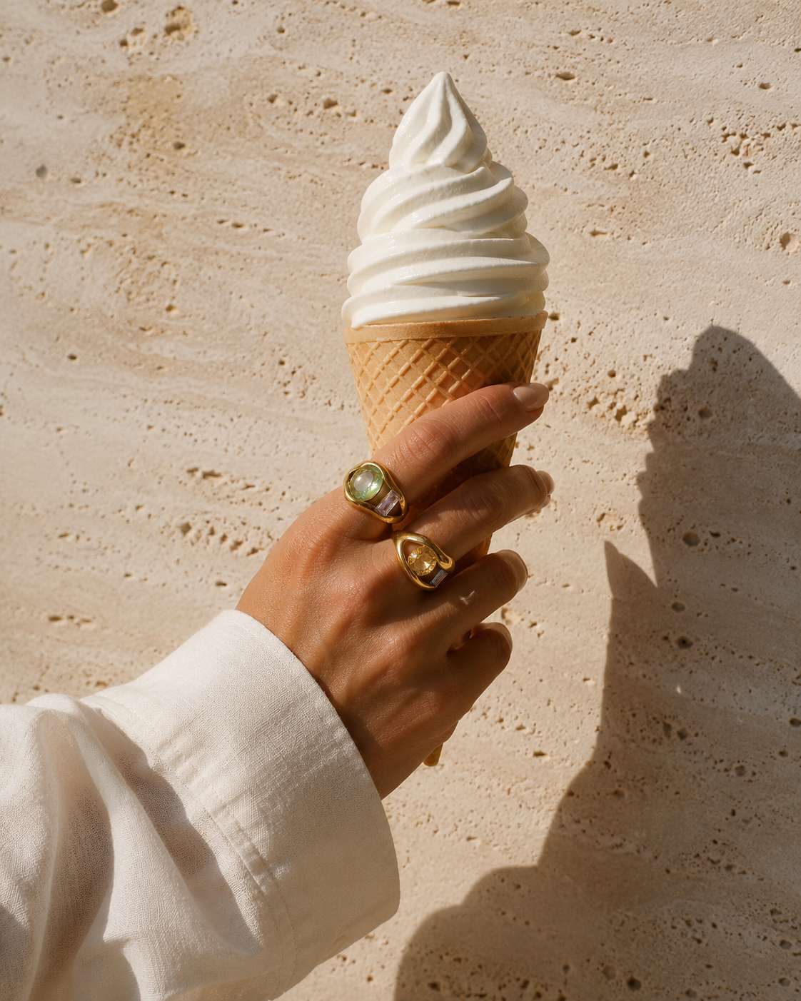 Model wears the gold Amara RING stacked with another colorful gem ring while holding a soft-serve ice cream cone in the sun.