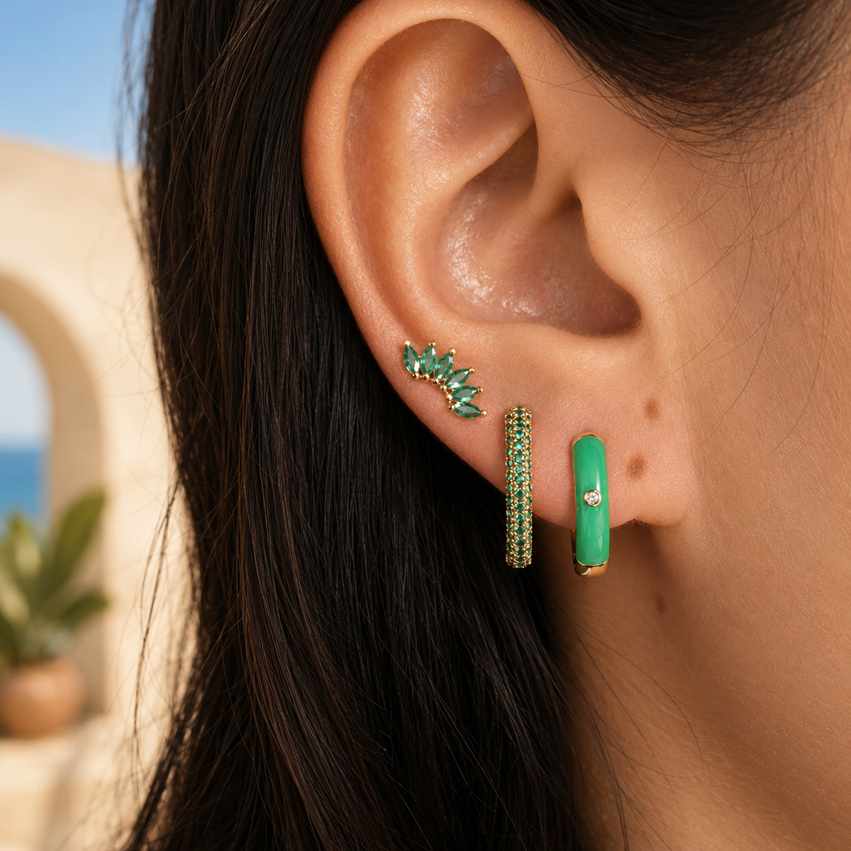 A model wears the three-piece Ames SET gold earrings in green: a marquise ear climber, a pave hoop, and a green enamel hoop.