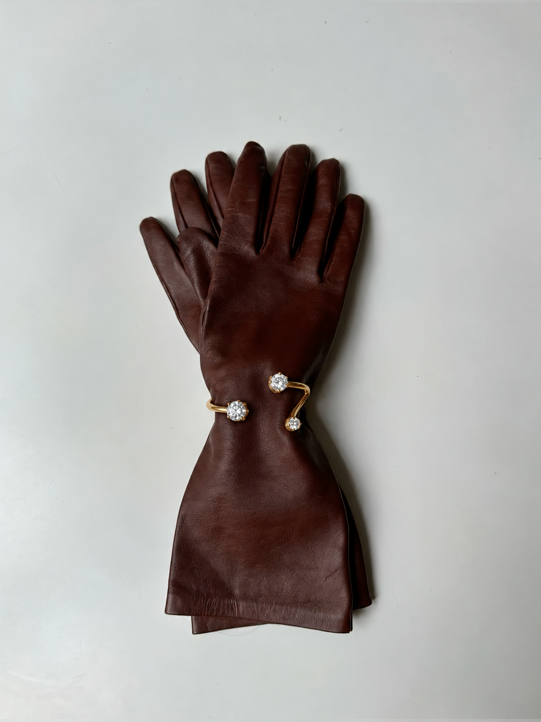 Gold Aurelia BRACELET cuff with sparkling zirconia ends styled on a brown leather glove against white — Folie à Trois wholesale
