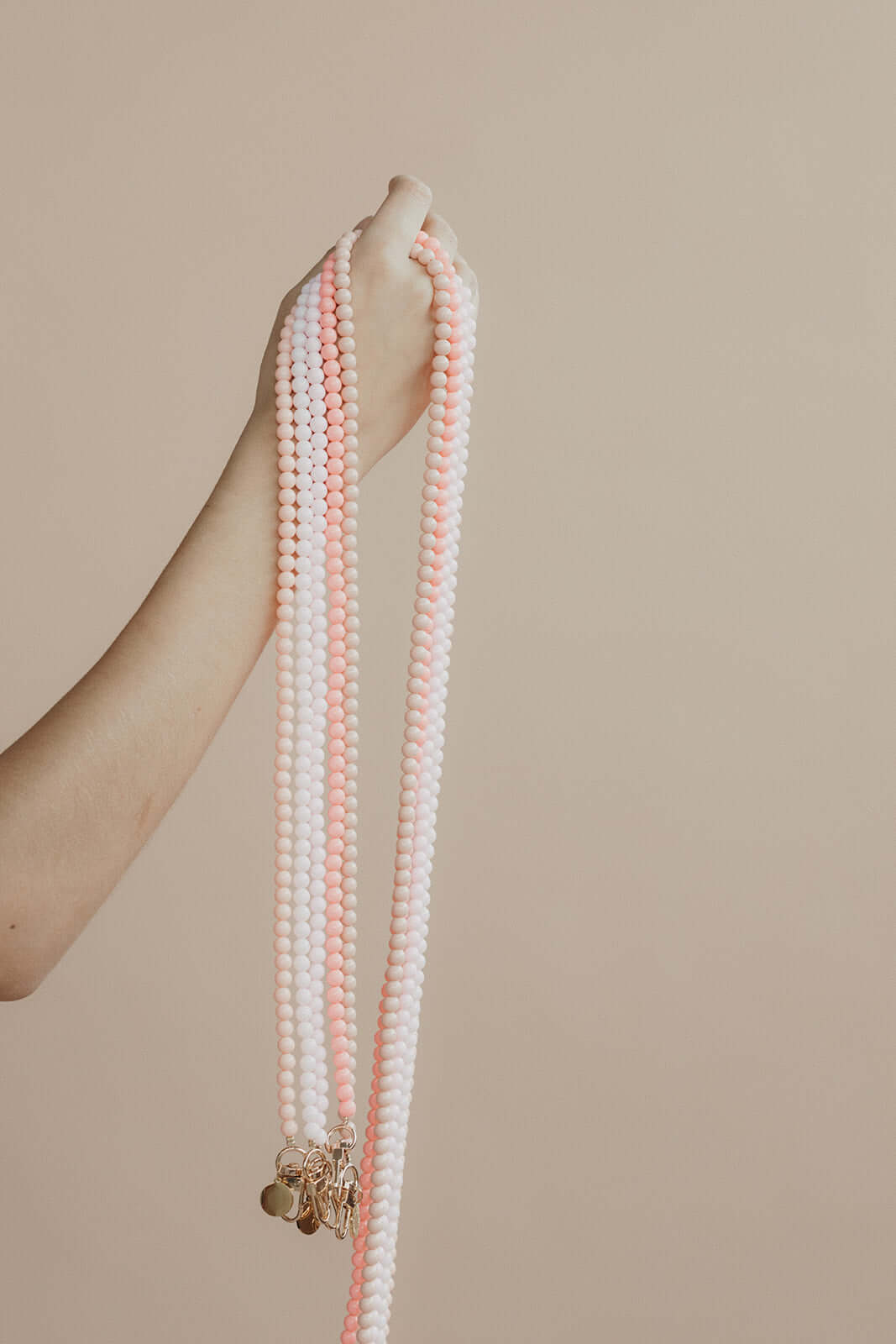 Close-up of a hand holding multiple pink and white beaded Aurora PHONE CORD strands.