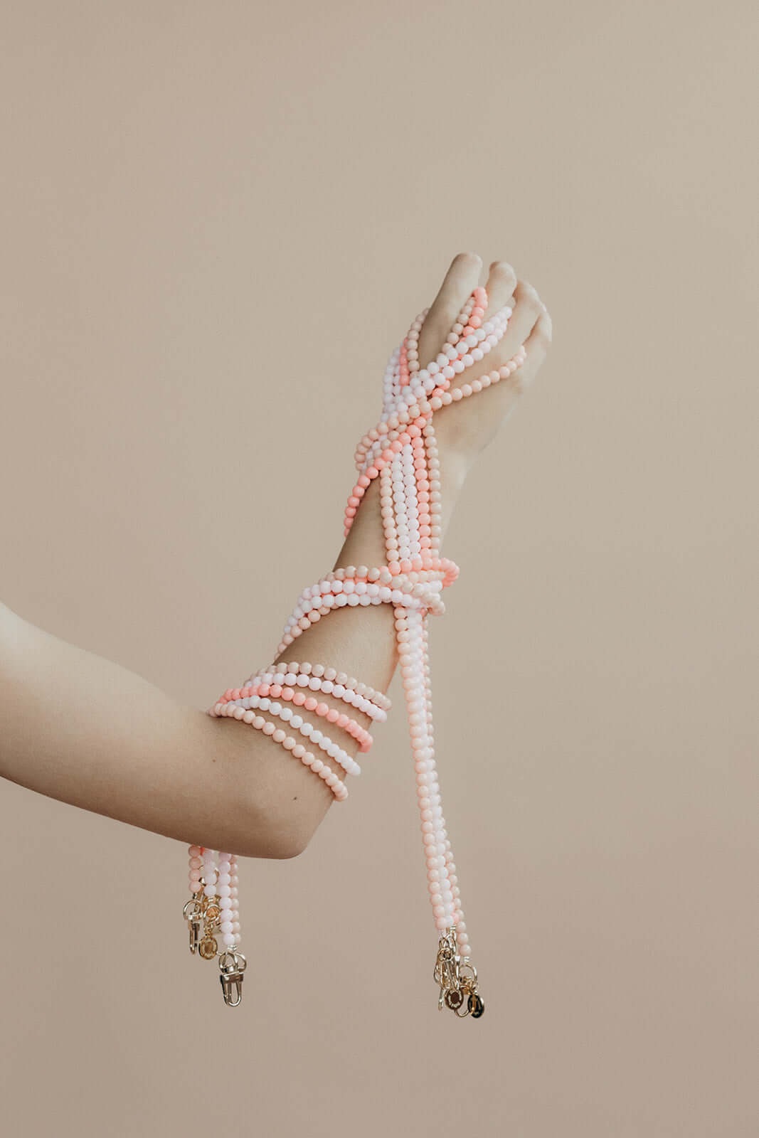 Model's arm wrapped in pink and white beaded Aurora PHONE CORD strands, worn like a bracelet.