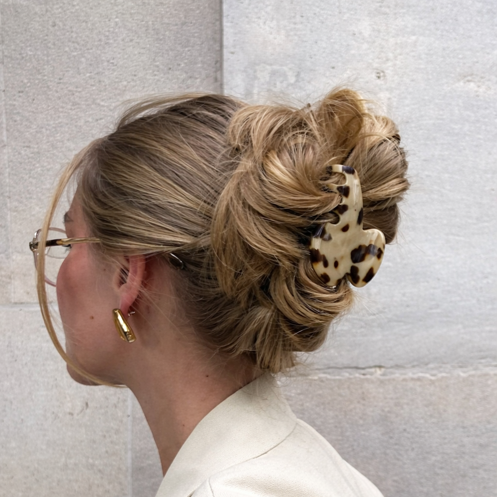 Baby Love HAIR CLIP's cream tortoiseshell claw clip worn in a low bun, photographed against a stone wall.