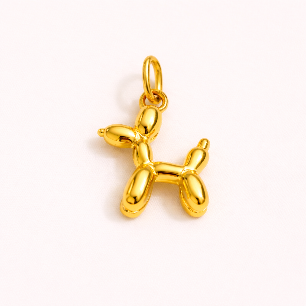 The Balloon Dog CHARM in a studio flat lay, a polished gold pendant shaped like a twisted balloon animal dog on cream fabric.