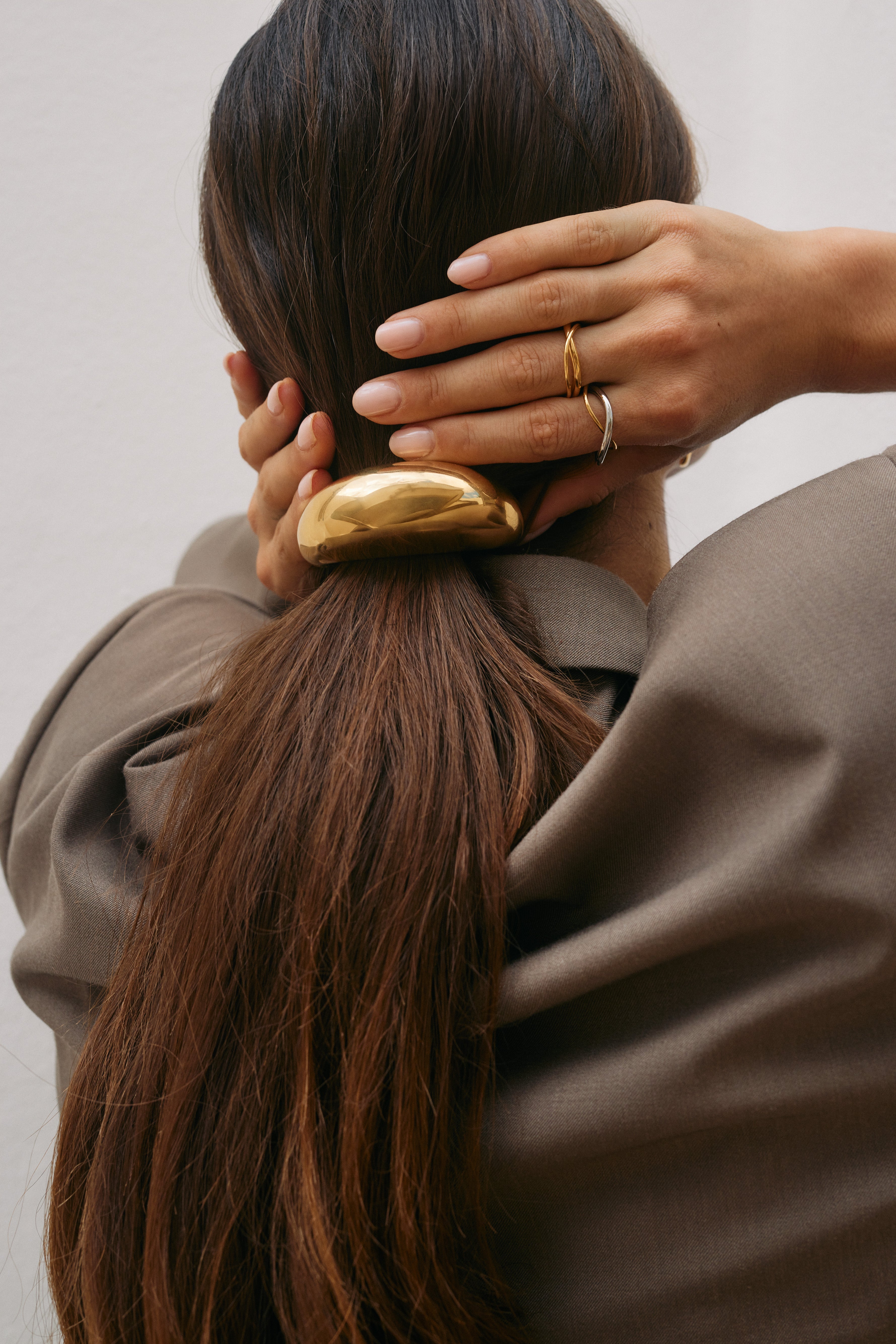 Close-up of a hand near the neck wearing the silver interwoven Belance RING stacked with a gold band, near a chunky gold hair clip.