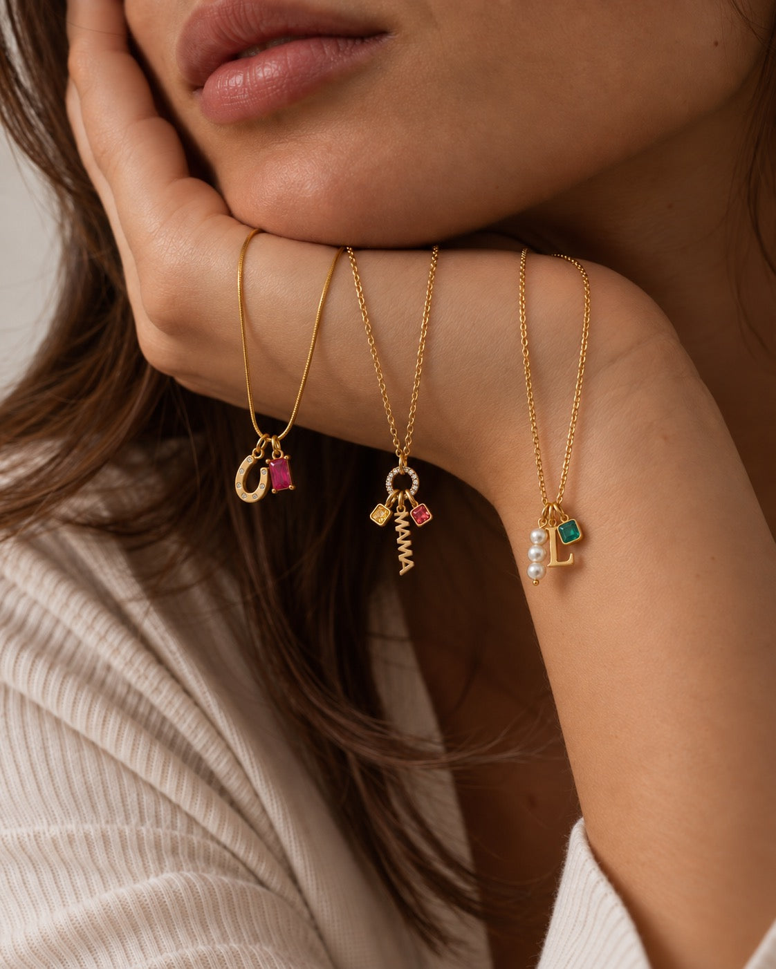 Model resting her chin on her hand wearing three gold necklaces with Birthstone CHARMS, initials and coloured gemstones