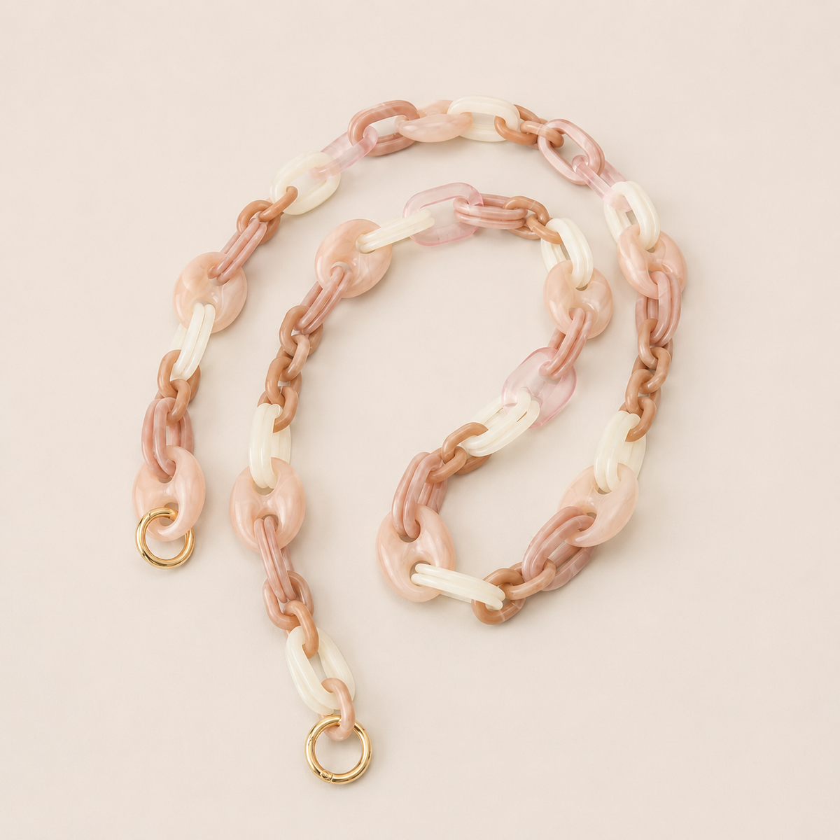 Folie à Trois Bracken long phone chain in pink, tan and white marbled links with gold clasps, coiled on a cream background.