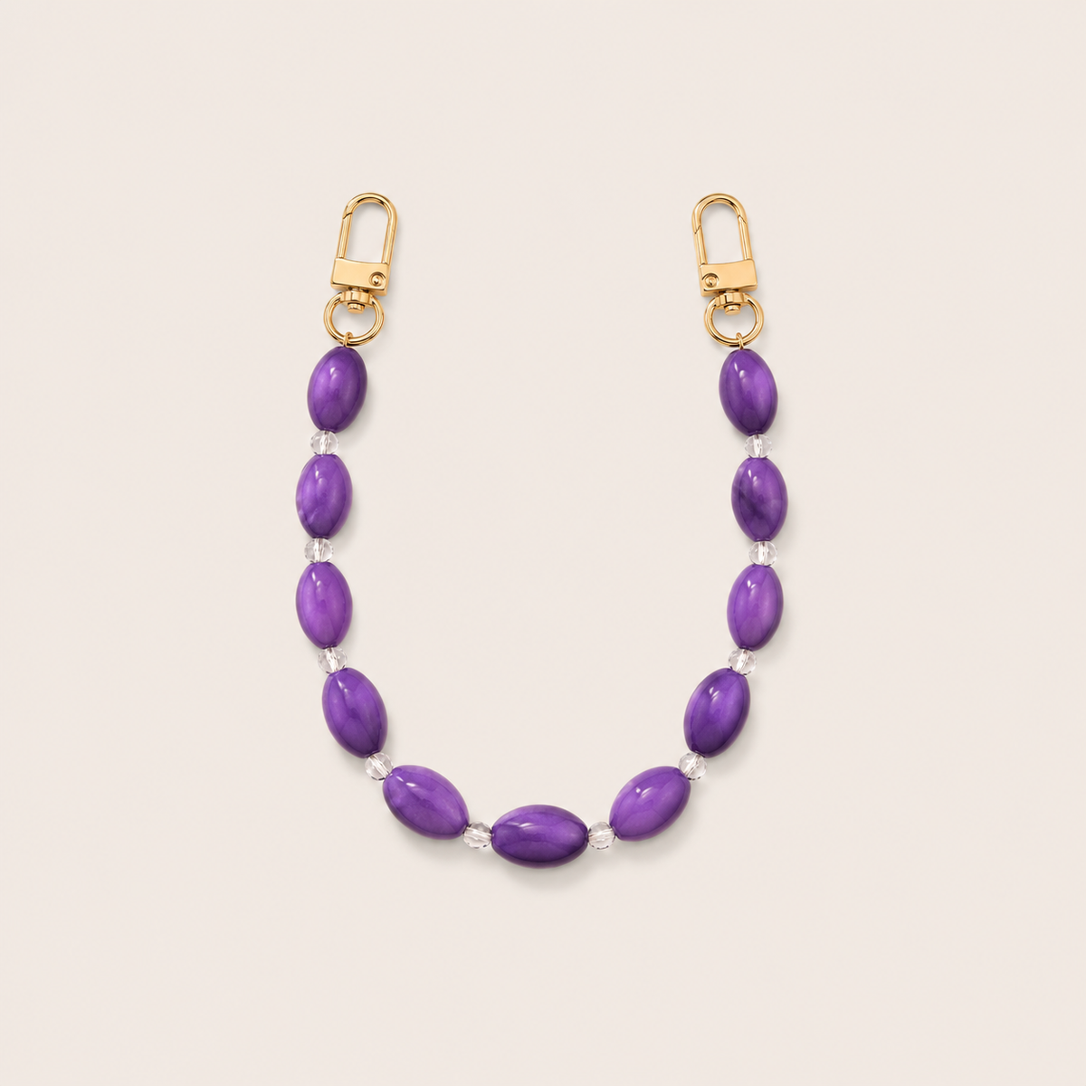Folie à Trois Bramble short wholesale phone chain in purple oval beads with clear glass spacers and gold clasps, laid flat on a cream background.