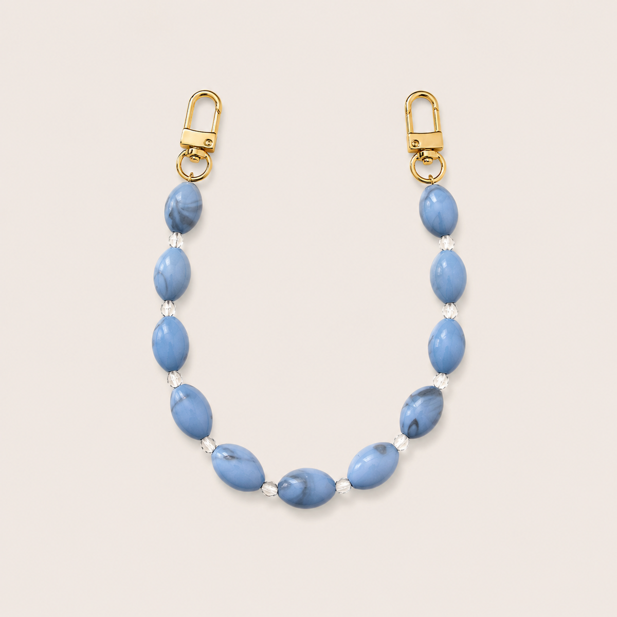 Folie à Trois Bramble short wholesale phone chain in blue marbled oval beads with clear glass spacers and gold clasps, laid flat on a cream background.