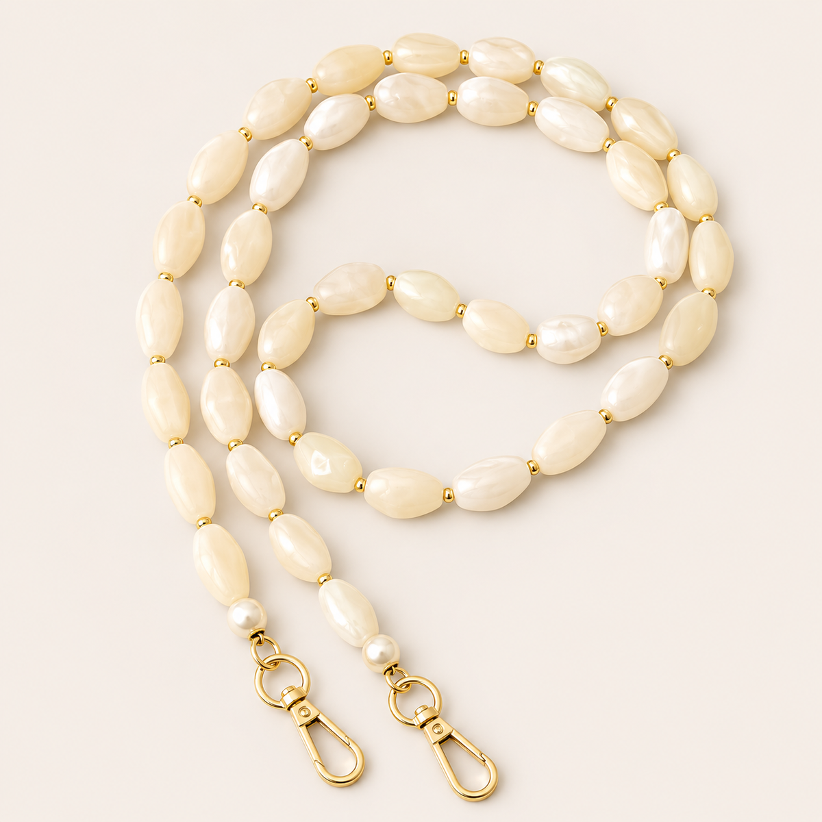 Folie à Trois Briar long phone chain in ivory pearlescent nugget beads with gold spacers, pearl accents and gold clasps, coiled on a cream background.