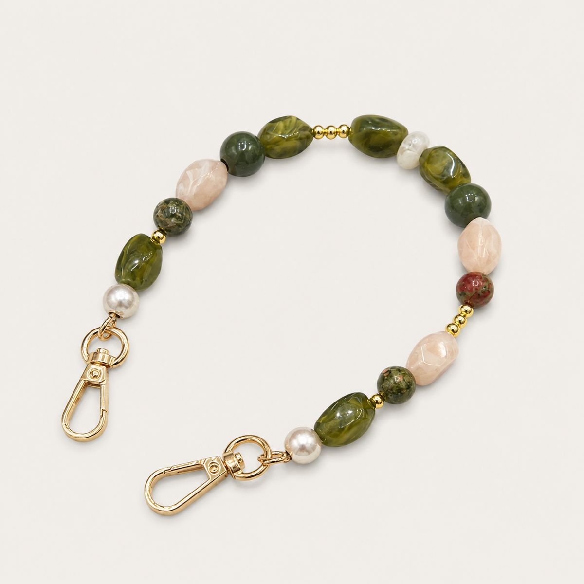Folie à Trois Briar short wholesale phone chain in mixed green, blush and pearl gemstone nugget beads with gold clasps, laid flat on a cream background.