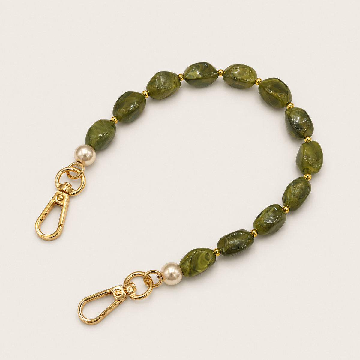 Folie à Trois Briar short wholesale phone chain in green marbled nugget beads with pearl accents and gold clasps, coiled on a cream background.