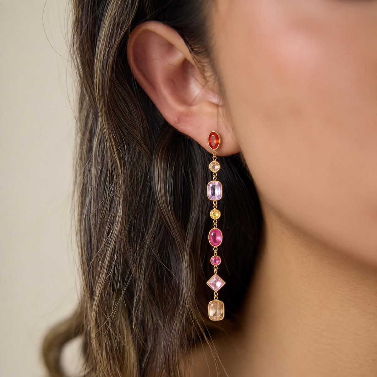 Model in profile wearing the gold Brise EARRINGS, a long linear drop of pink, orange, peach and yellow bezel-set gemstones.