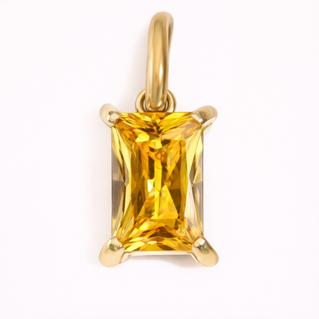 Close-up of the Classic Drop Charm in a golden citrine stone, set in a gold prong mount on a cream background.
