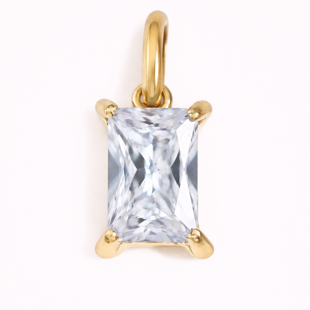 Close-up of the Classic Drop Charm in a clear white cubic zirconia stone, set in a gold prong mount on a cream background.