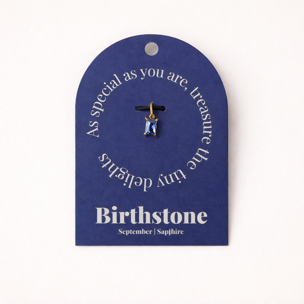 The Classic Drop Birthstone Charm in blue sapphire hangs from a black cord on a navy gift card reading Birthstone, September, Sapphire.