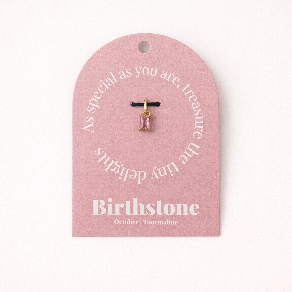 The Classic Drop Birthstone Charm in pink tourmaline hangs from a black cord on a dusty pink card reading Birthstone, October, Tourmaline.