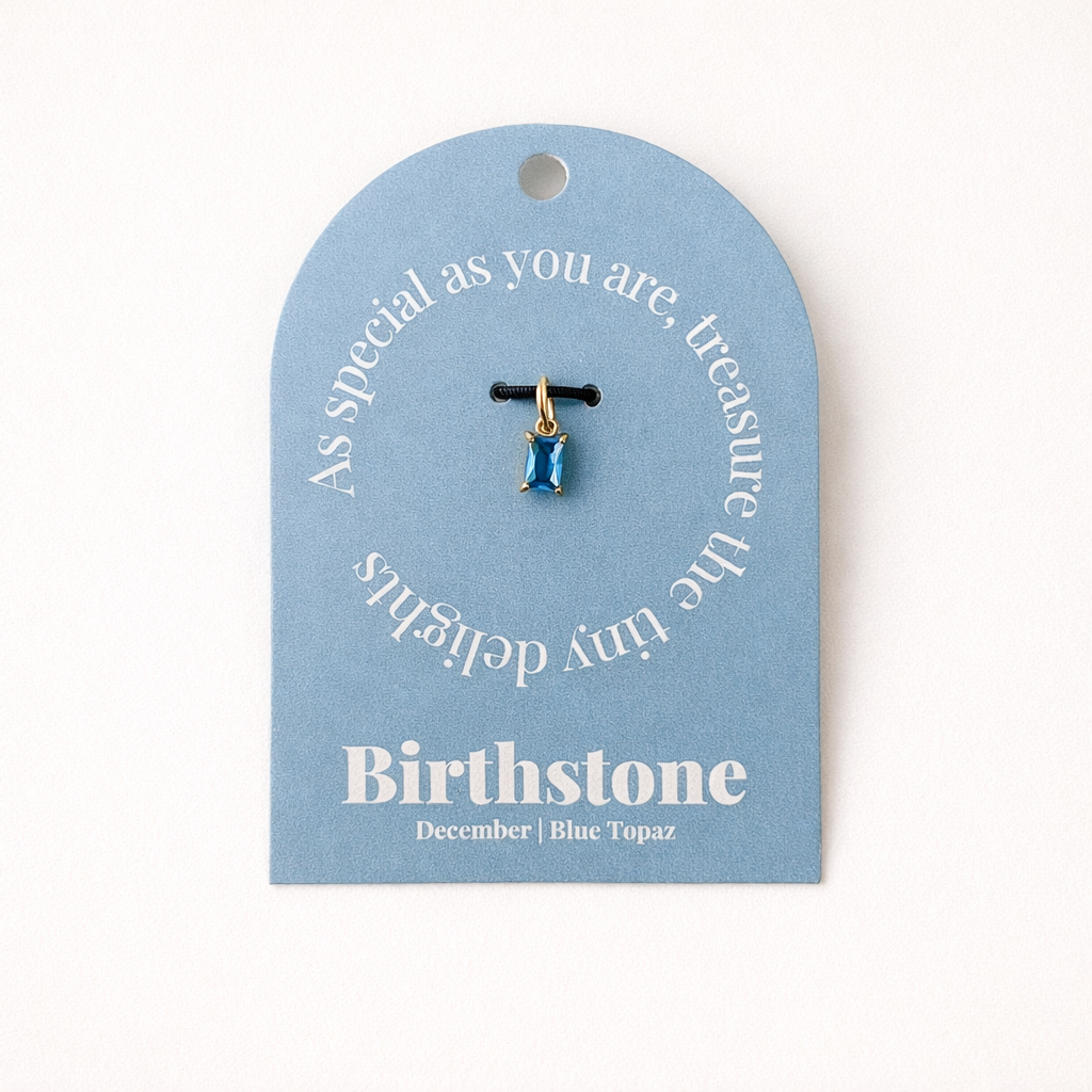 The Classic Drop Birthstone Charm in blue topaz hangs from a black cord on a light blue card reading Birthstone, December, Blue Topaz.
