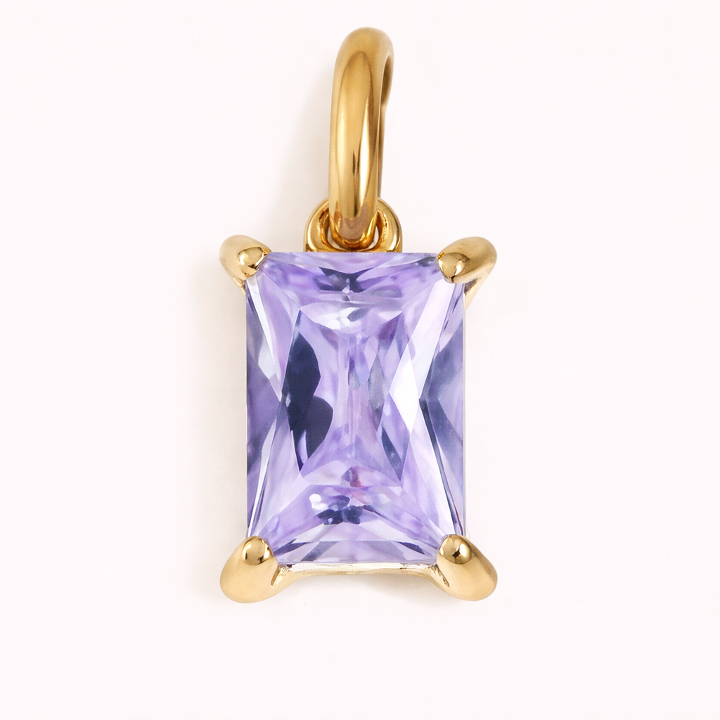 Close-up of the Classic Drop Charm in a soft lavender purple stone, set in a gold prong mount on a cream background.
