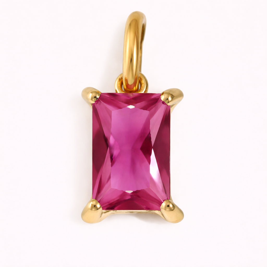 Close-up of the Classic Drop Charm in a vibrant pink magenta stone, set in a gold prong mount on a cream background.
