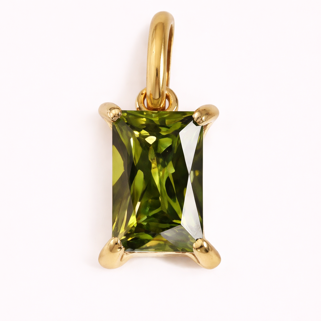 Close-up of the Classic Drop Charm in an olive green stone, set in a gold prong mount on a cream background.