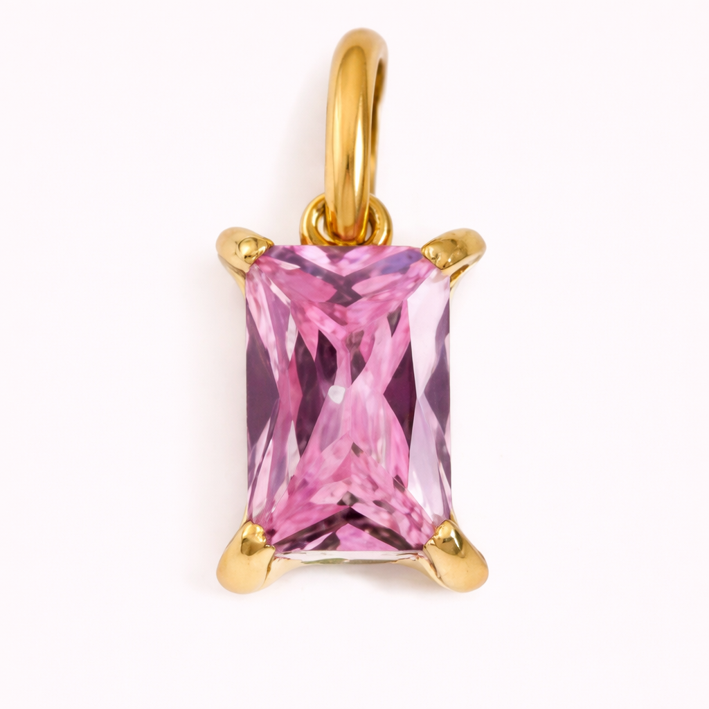 Close-up of the Classic Drop Charm in a soft pink stone, set in a gold prong mount on a cream background.