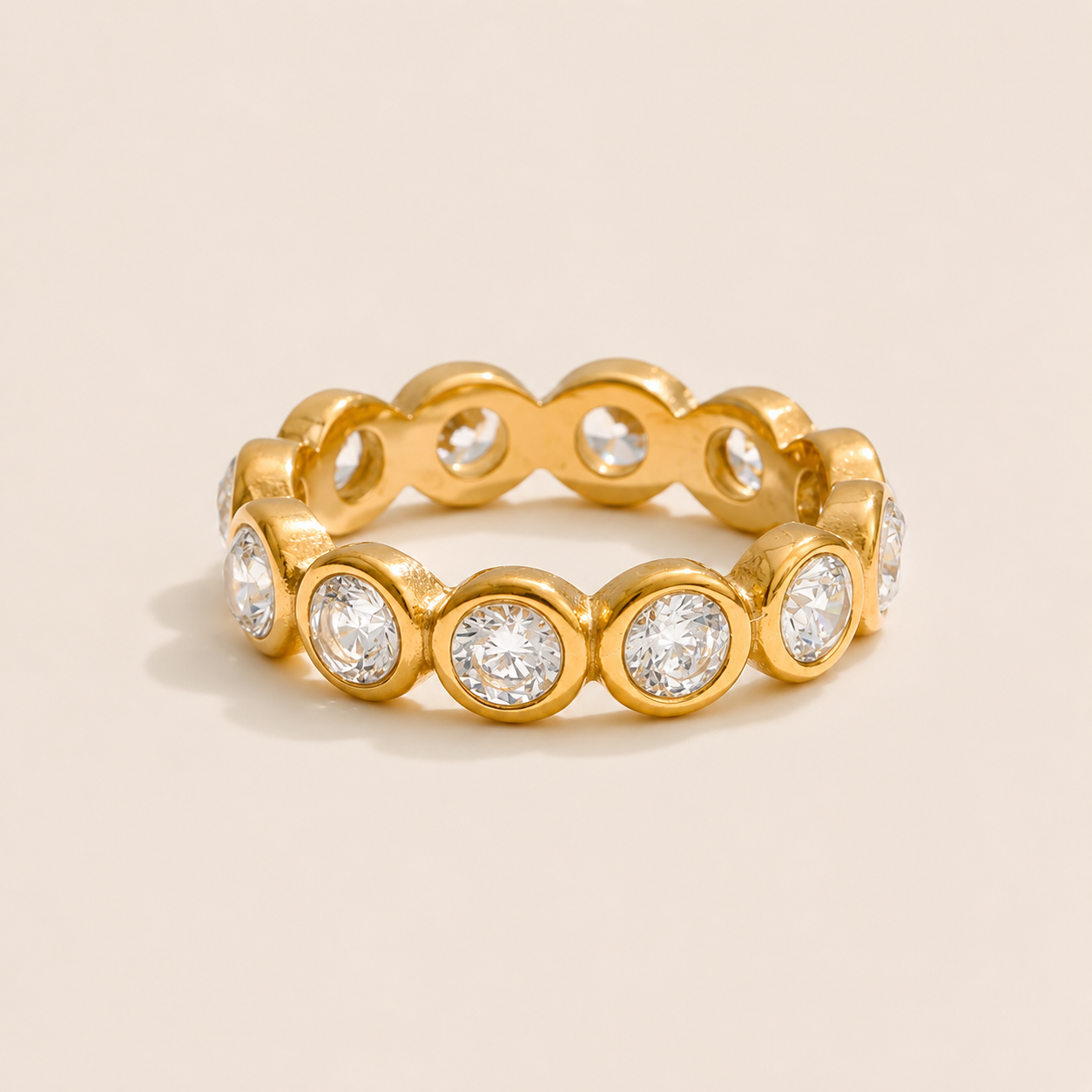 Gold eternity ring set edge to edge with round bezel-set white zirconia stones, shown on a cream backdrop — Folie à Trois Club Soleil RING.