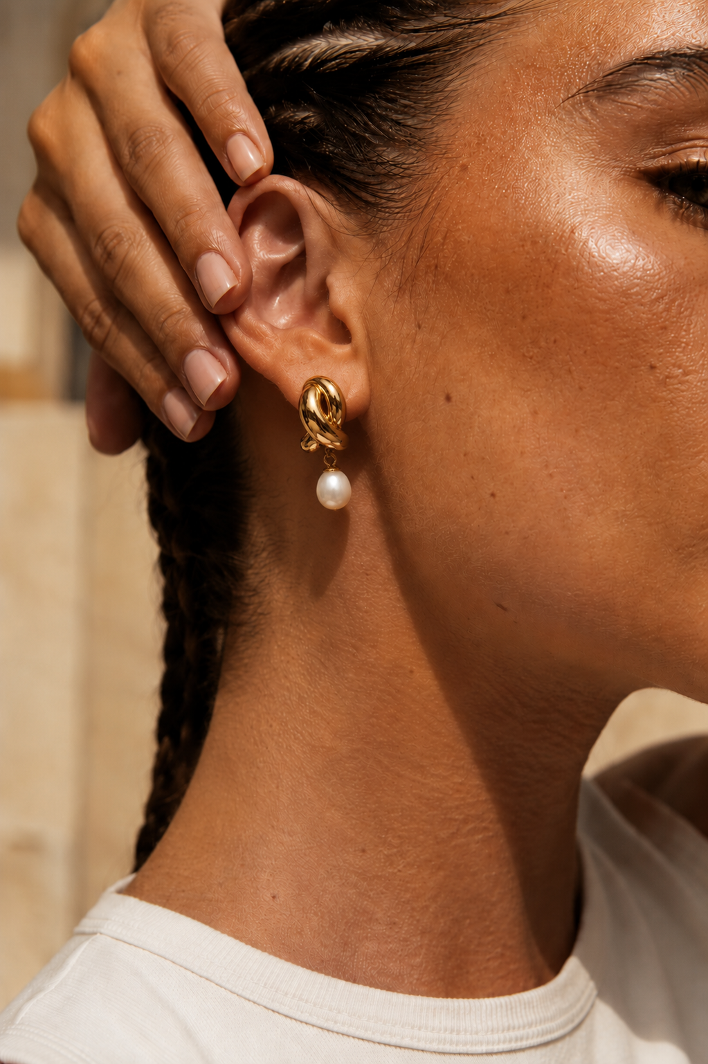Model wears the gold Folie à Trois Cruz EARRINGS, a twisted knot stud with a dangling pearl drop, in a close-up beauty shot.