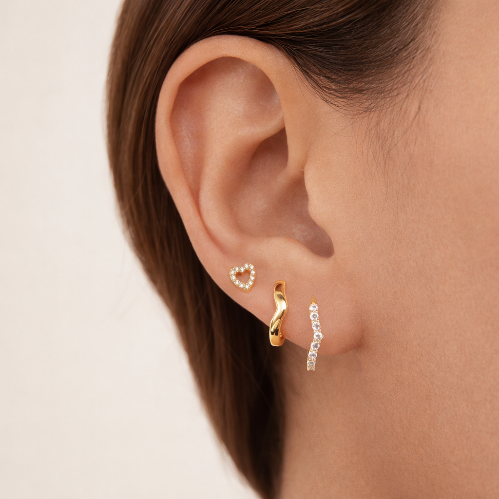 Delia Set worn on the ear in gold, a pave heart stud paired with a wavy hoop and a pave chevron hoop.