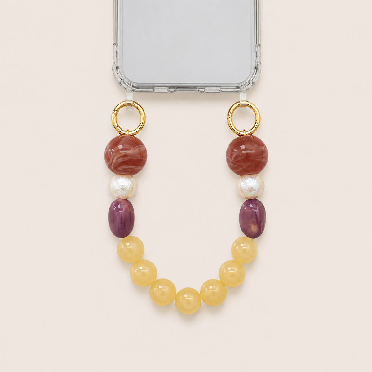 Red, pearl, purple, and yellow bead phone chain clipped to a clear iPhone case on cream — Folie à Trois Delphine short phone chain