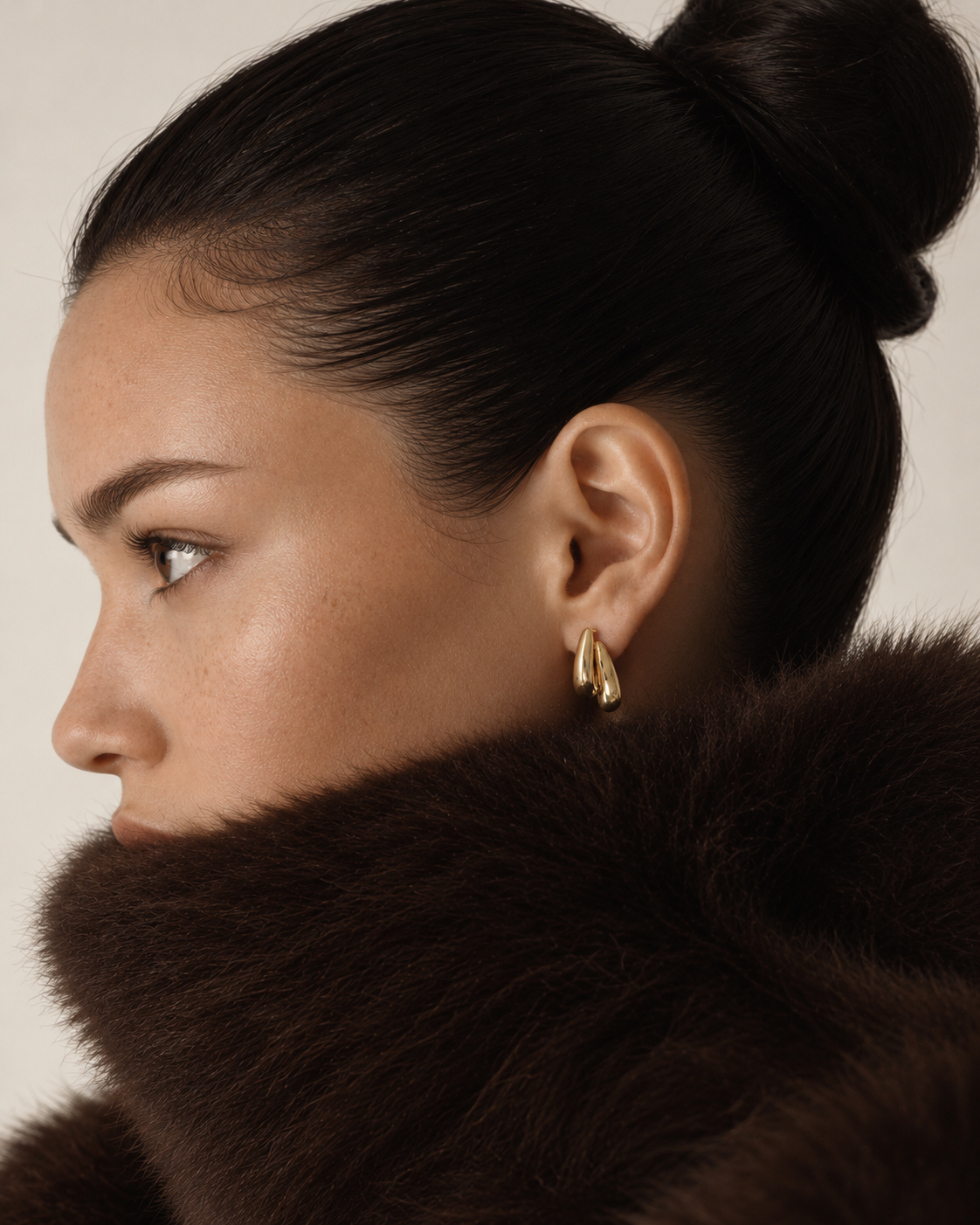 Profile of a model with a sleek bun and brown fur collar wearing a gold Doppia EARRINGS hoop — Folie à Trois wholesale