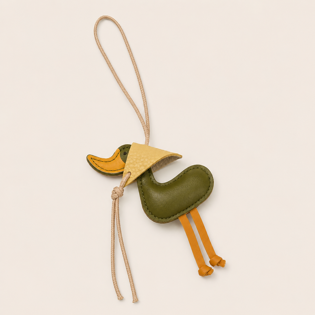 Olive green leather duck-shaped bag charm with a cream cord loop and yellow beak and feet, Folie à Trois Duckling BAG CHARM on a neutral background.