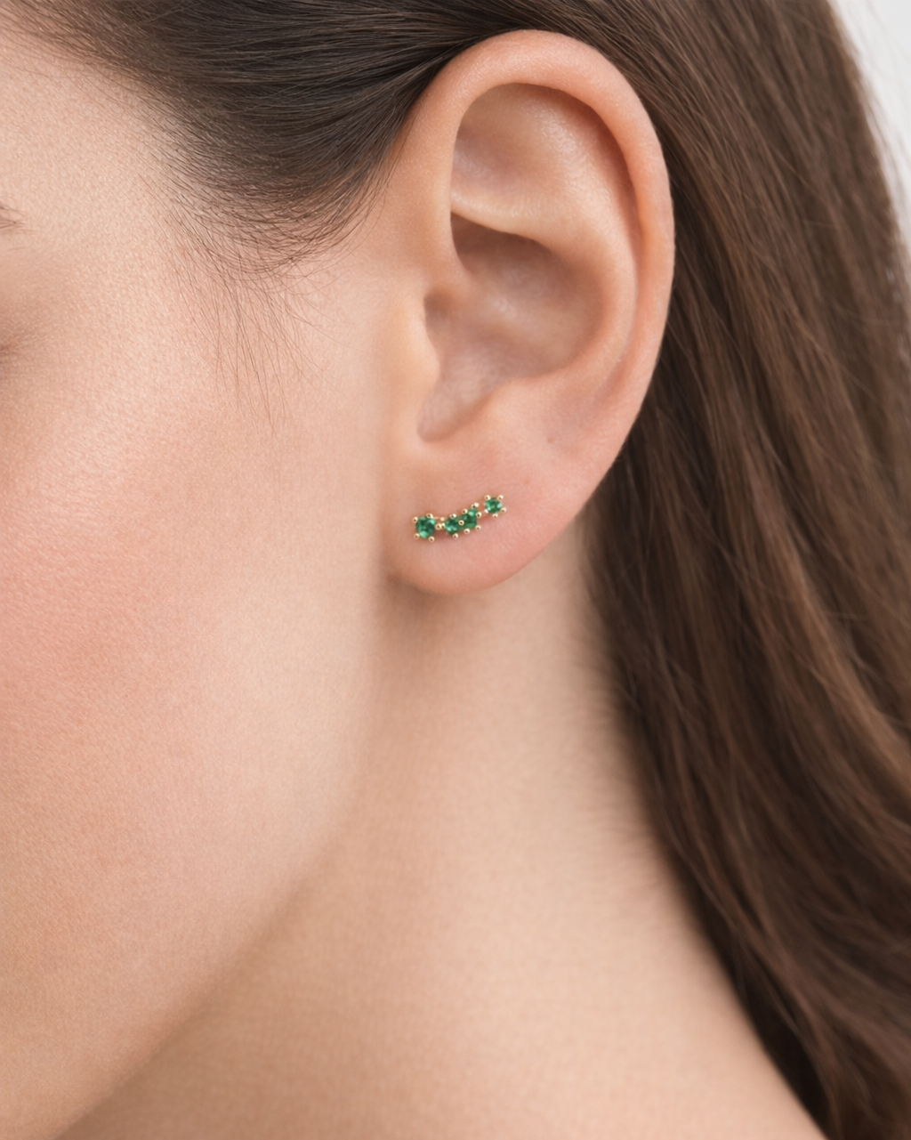 Emerald-green climber earring worn on the ear, showing the curved three-stone design set close along the upper lobe.