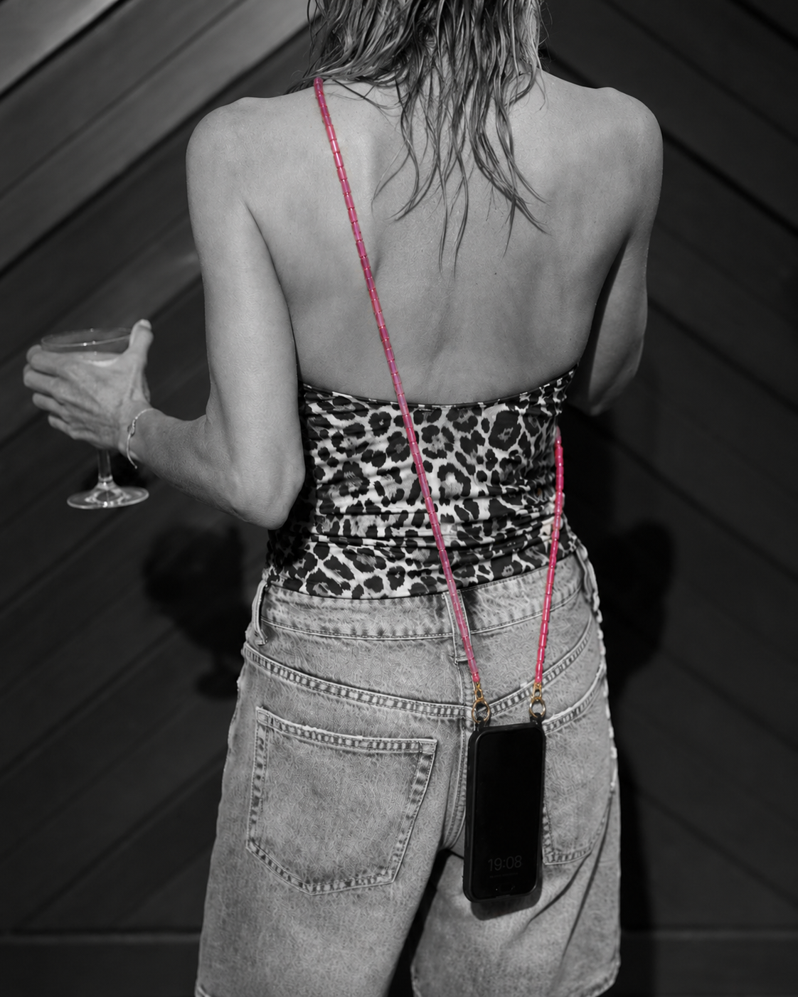 Black-and-white shot of a woman in a leopard top holding a cocktail, phone worn crossbody on a pink beaded chain — Folie à Trois Elowen phone chain