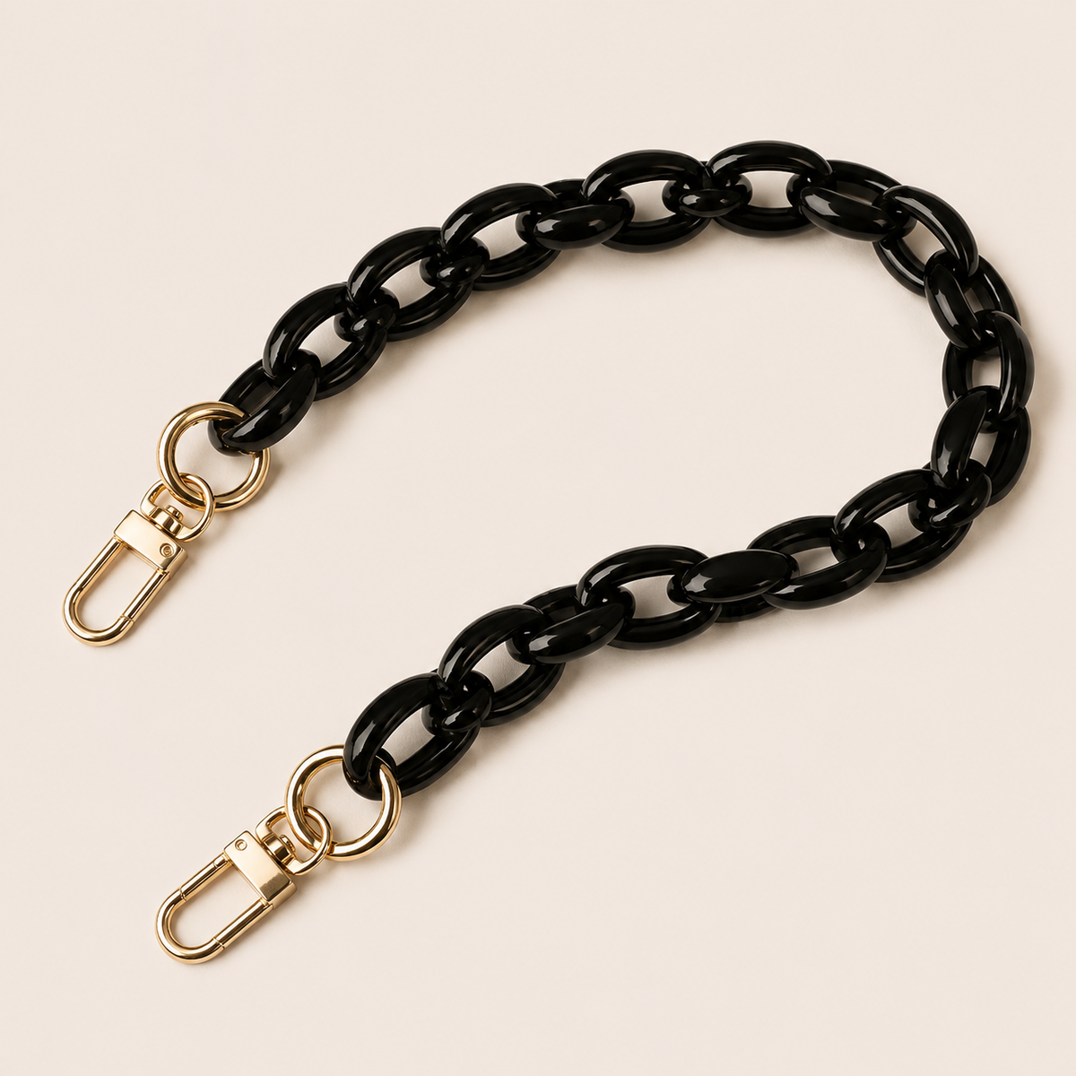 The Ember SHORT PHONE CHAIN in glossy black acrylic with gold-tone lobster clasp ends, curved on a light beige background.