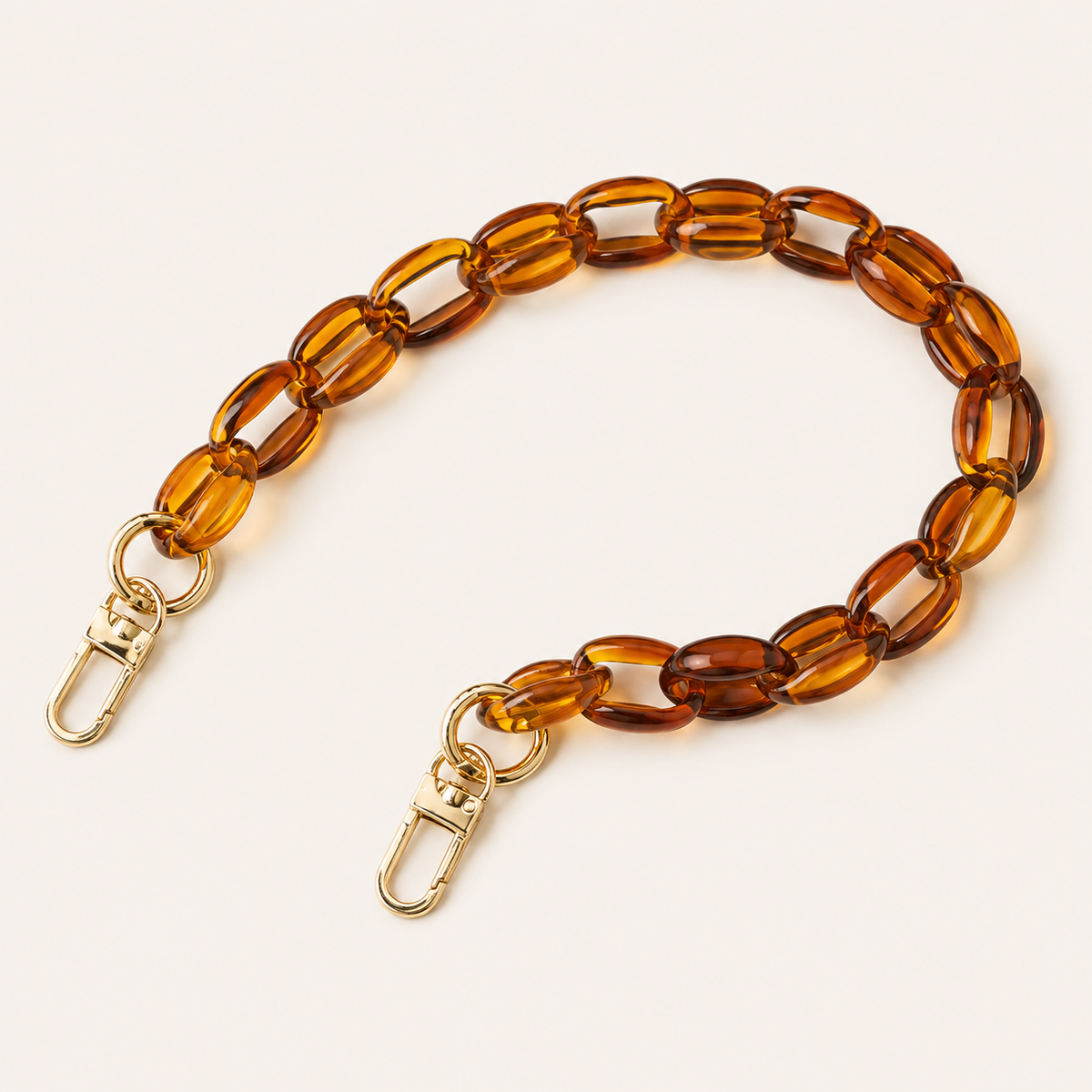 The Ember SHORT PHONE CHAIN in amber transparent acrylic with gold-tone lobster clasp ends, curved on a light beige background.