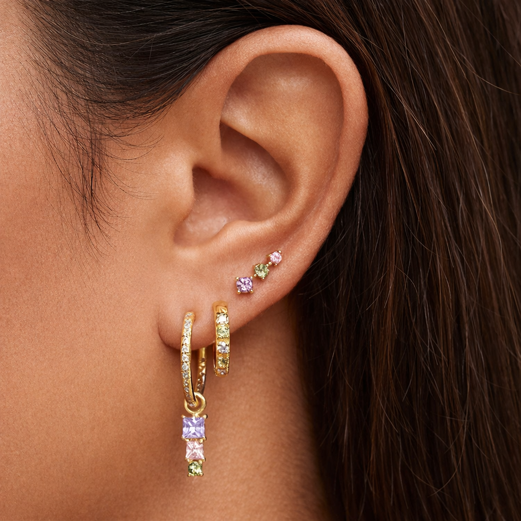 Worn layered along the ear, Fashion House SET shows its stud, colorful hoop, and dangling square-stone hoop.