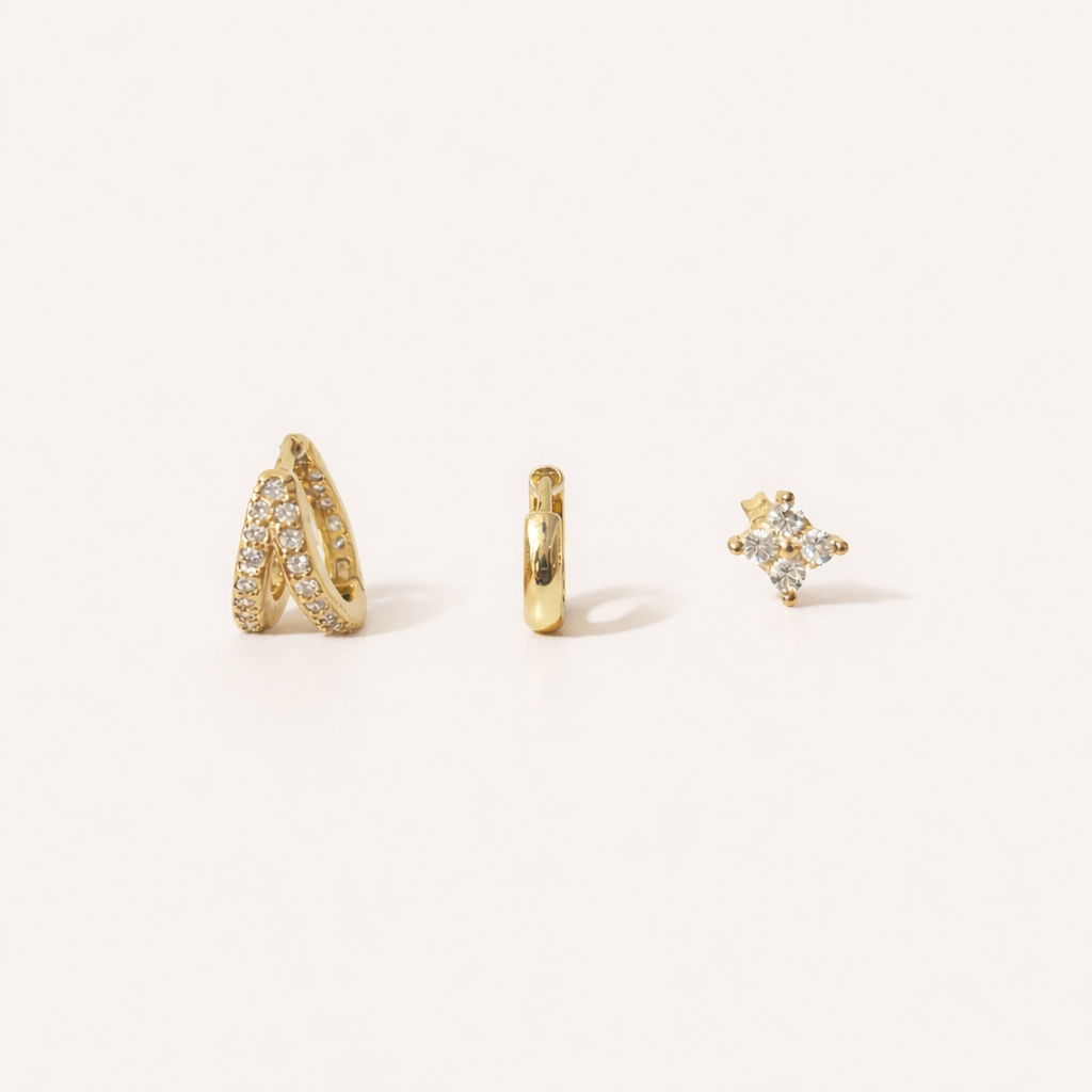 Faye Set of gold jewelry, a pave crossover hoop, a plain huggie hoop, and a four-point crystal stud, laid flat.