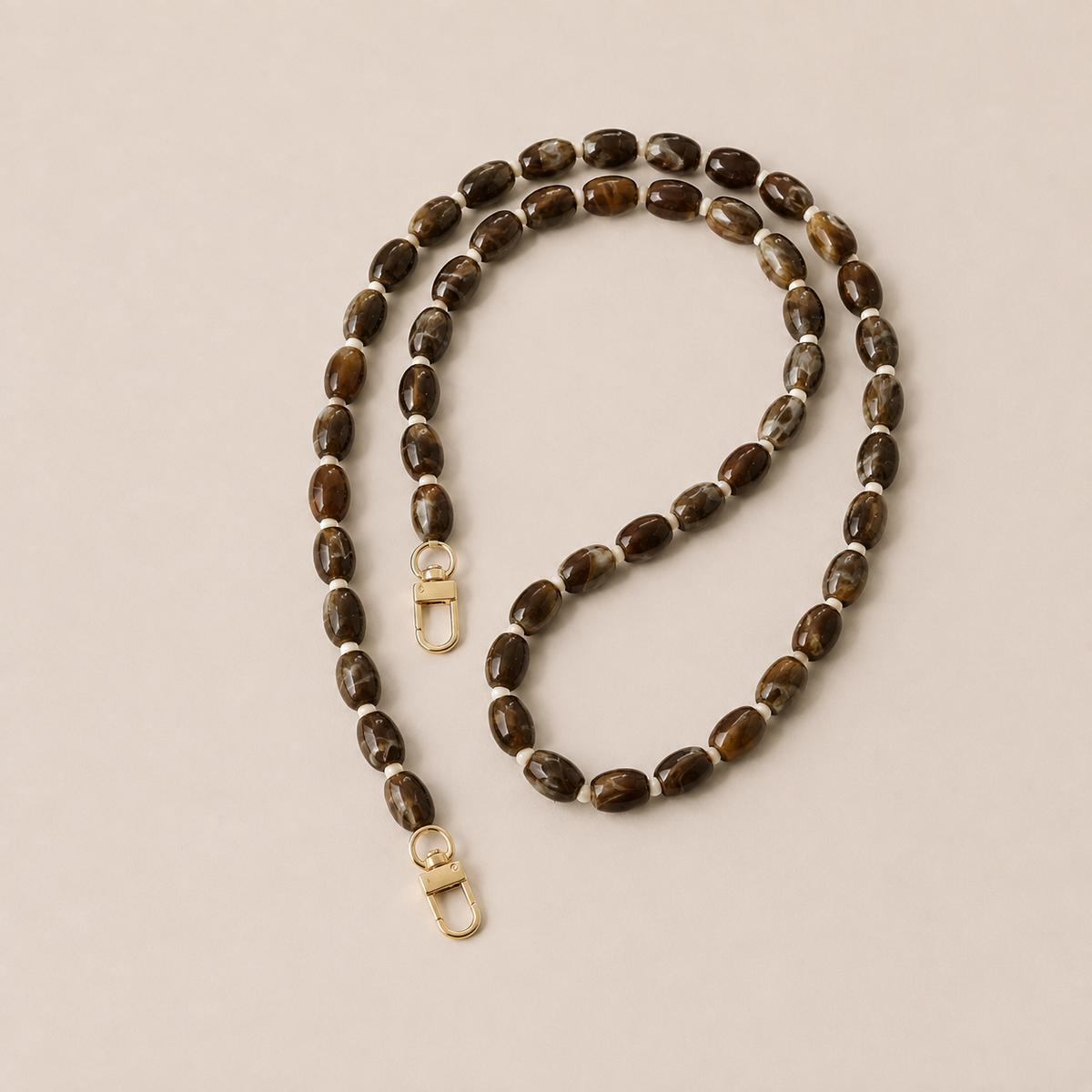 Folie à Trois Fennel long phone chain in brown marbled oval beads with cream spacers and gold clasps, laid flat on a cream background.