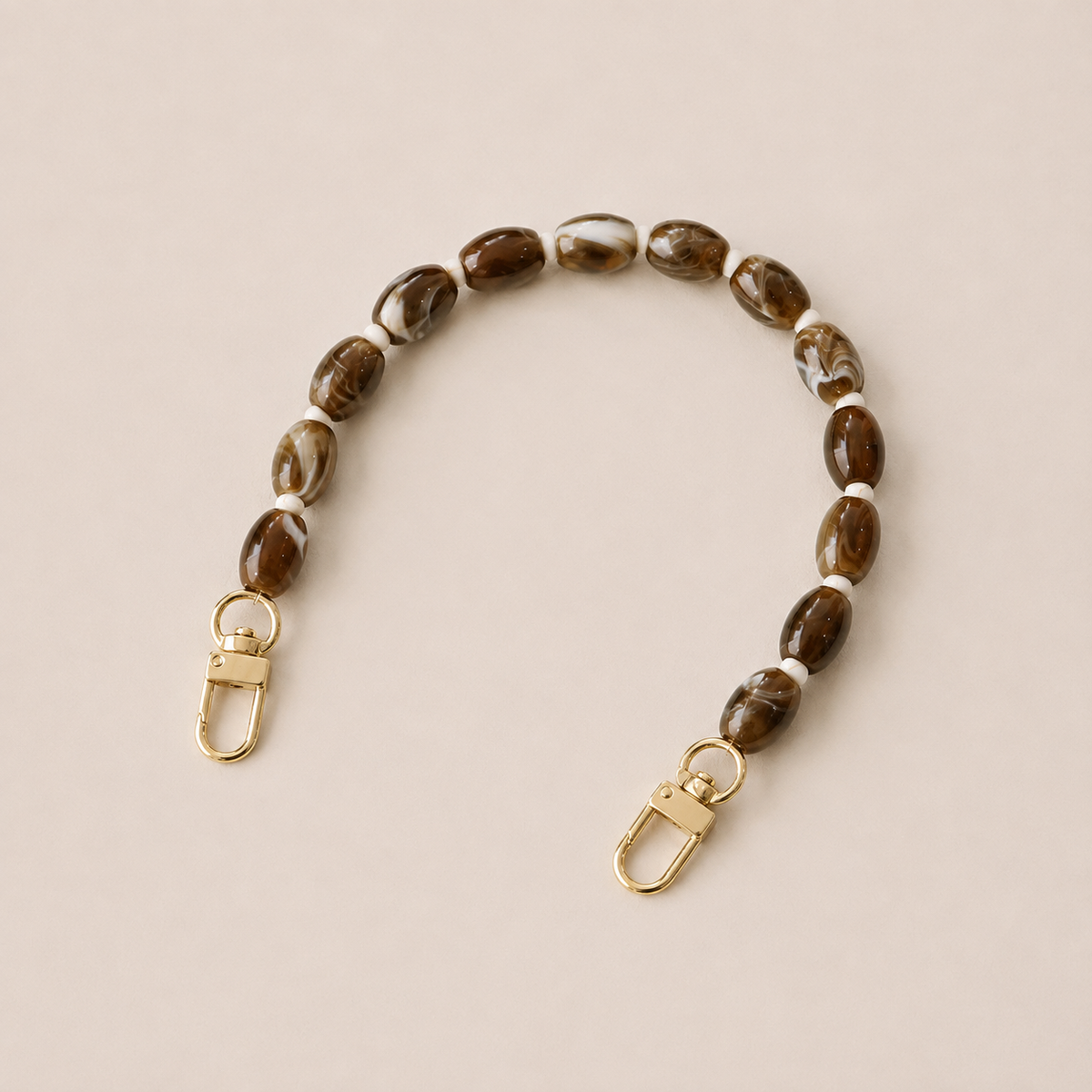 Folie à Trois Fennel short wholesale phone chain in brown marbled oval beads with cream spacers and gold clasps, laid flat on a cream background.