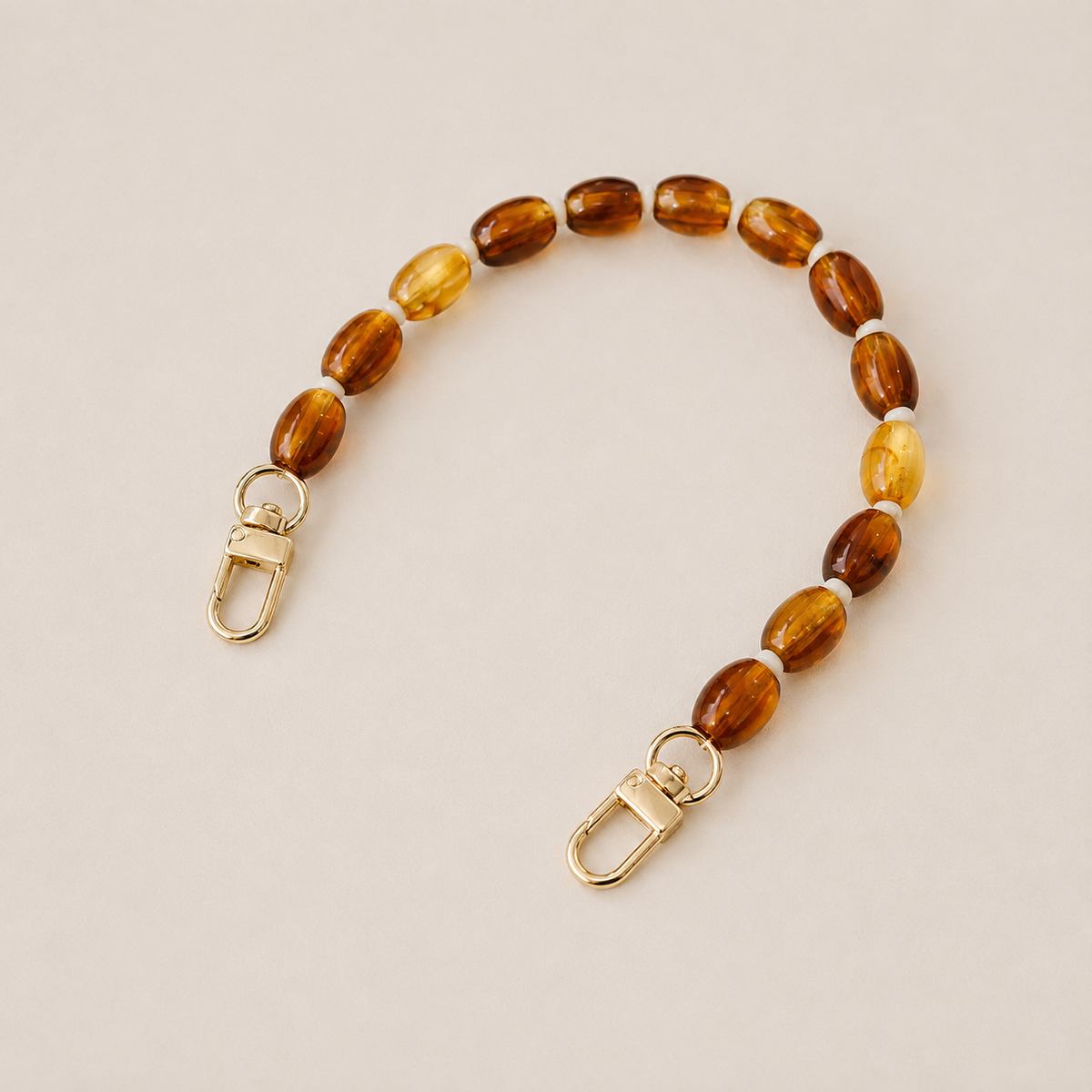 Folie à Trois Fennel short wholesale phone chain in amber oval beads with cream spacers and gold clasps, laid flat on a cream background.