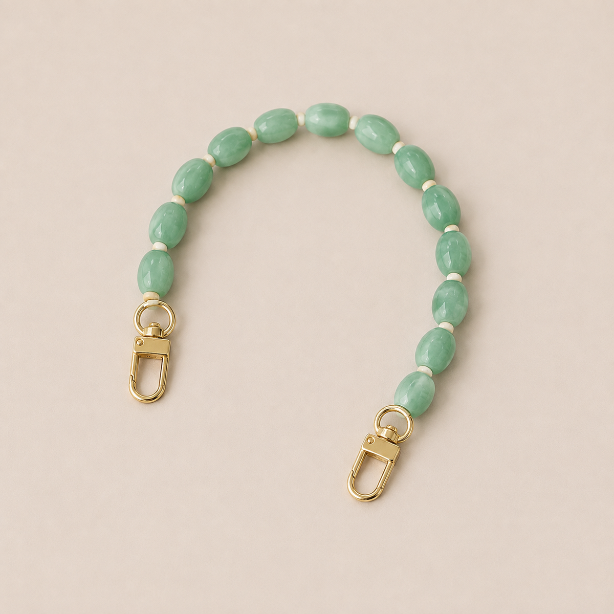 Folie à Trois Fennel short wholesale phone chain in jade green oval beads with cream spacers and gold clasps, laid flat on a cream background.